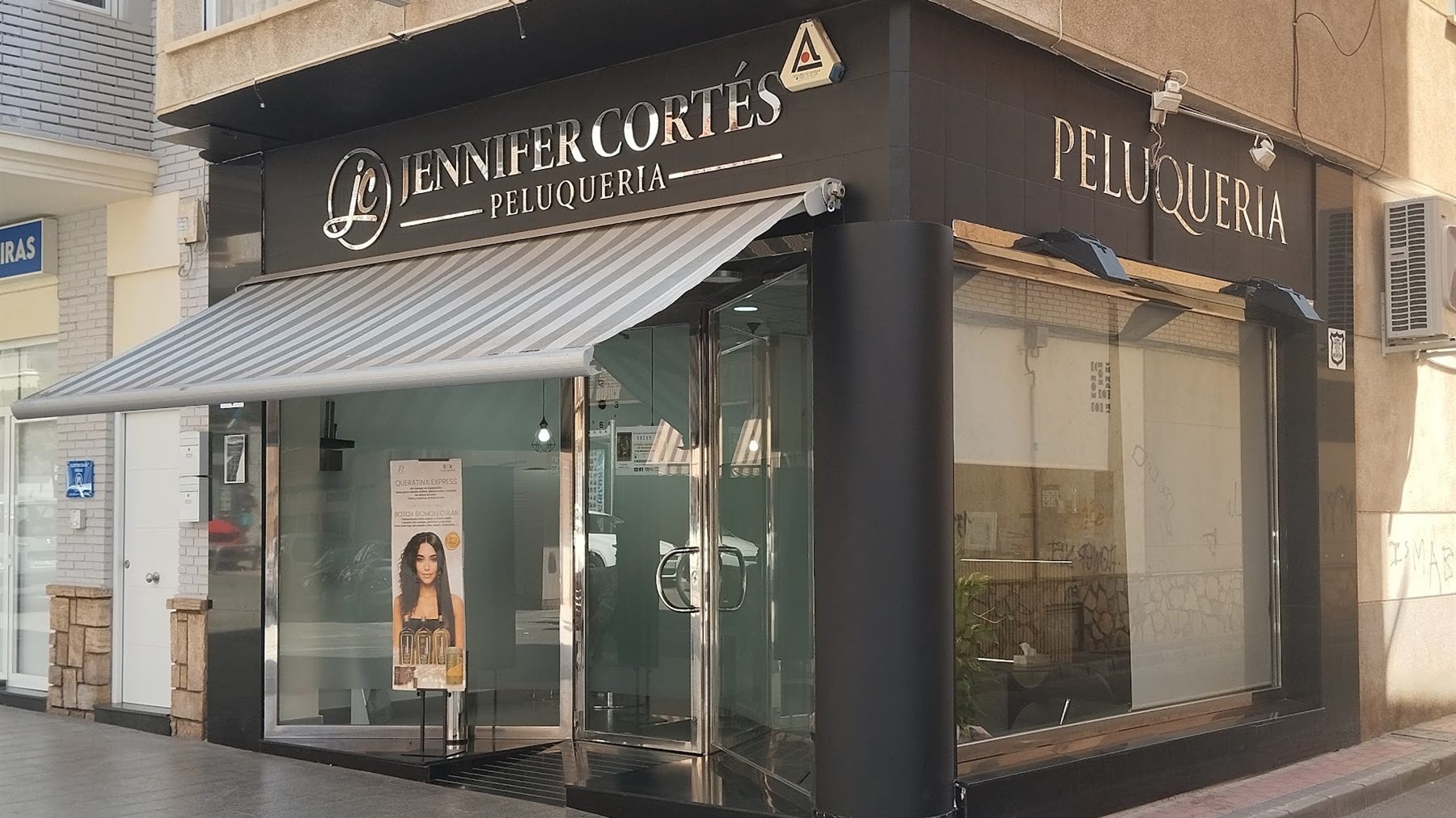 Fachada de la peluquería Jennifer Cortés en la avenida Juan Carlos I de Águilas: local en esquina, fachada negra y rótulo dorado.