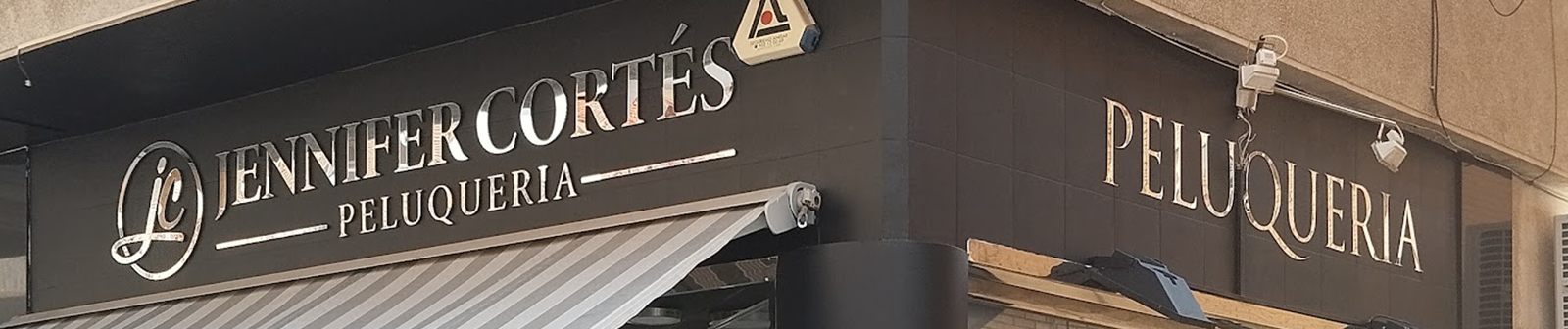 Detalle del rótulo dorado sobre fondo negro: monograma jc, «Jennifer Cortés» y «Peluquería».